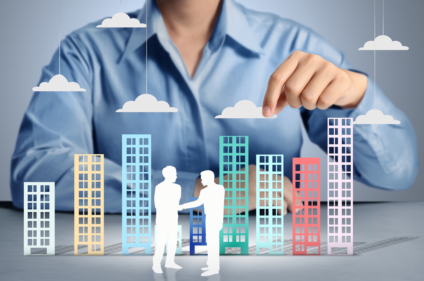 two human figures shaking hands against a backdrop of building-shaped paper cutouts