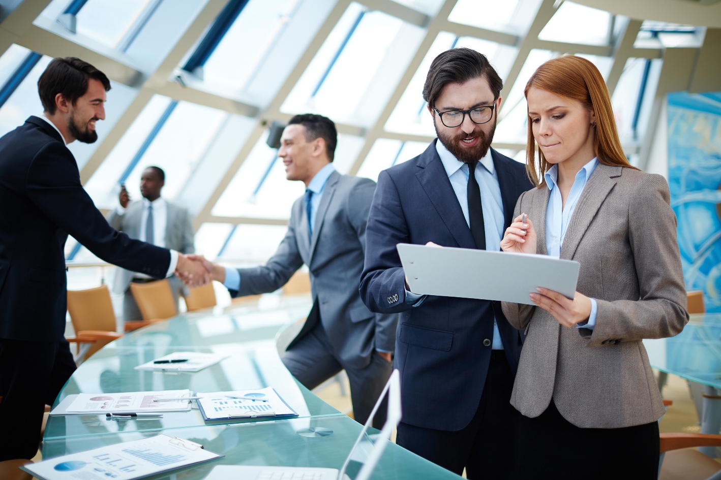 two people in business attire discuss a document while two others shake hands